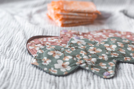 Reusable cloth menstrual pads with floral patterns in pink and green tones placed on a textured...