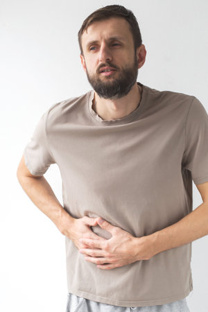 Man suffering from stomach pain, holding his abdomen with both hands. expression on face shows discomfort, possibly due to indigestion, food poisoning, or illness. Concept of health, pain, verticalの写真素材