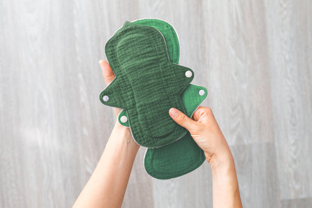 Reusable cloth menstrual pads in green color held by a woman's hands against a neutral background. Concept of women's health, sustainability, and eco-friendly lifestyleの写真素材