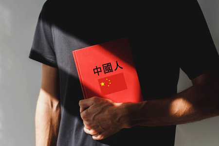 A person wearing a black t-shirt holds a red Chinese language textbook with Chinese characters and a...