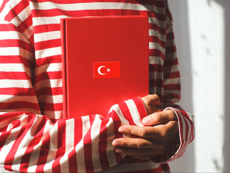 One girl, whose face is not visible in a striped red long sleeve, holds a red Turkish language textbook with Turkey flag, foreign language learning concept.の写真素材