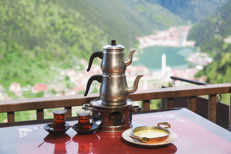 Traditional Turkish tea set with two glasses and Muhlama dish on a table, overlooking the scenic mountain lake Uzung l in the Black Sea region of Turkey.の写真素材