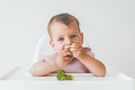 baby's first feeding eating broccoli food by himself on baby high chair and making mess