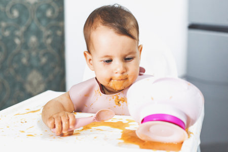 messy baby sits in a highchair and eats lure vegetable puree soup, the concept of baby food and childhood.の写真素材