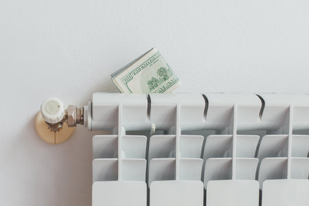 a stack of money dollars on a white battery heating radiator on a white wall, the concept of saving utility bills, Energy crisisの写真素材