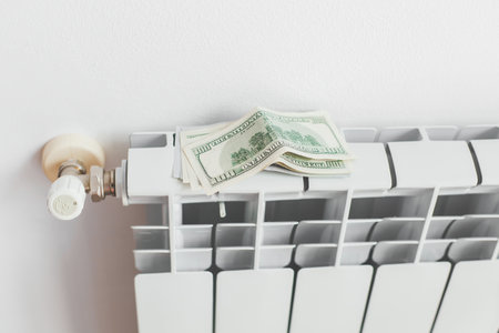 a stack of money dollars on a white battery heating radiator on a white wall, the concept of saving utility bills, Energy crisisの写真素材