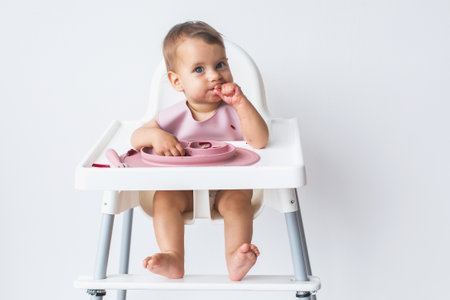 baby sits in a high chair in full growth eats complementary foods on a white background.の写真素材