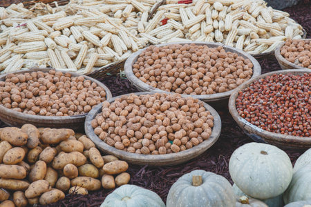 Rustic market display with wooden bowls filled with walnuts and hazelnuts, surrounded by potatoes, pumpkins, and dried corn, representing autumn harvest and organic farmingの写真素材
