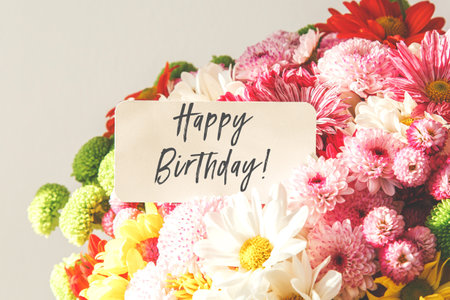bright bouquet of multi-colored chrysanthemum and gerbera flowers with a white greeting card with the text happy birthdayの写真素材