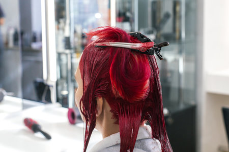 hairdresser colorist client sits in a chair with his back turned, hairdresser dyes hair red, bleaches hair roots in beauty salon, concept of beauty and hairdressing training. hair clipsの写真素材