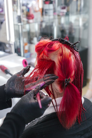 close-up hairdresser colorist dyes client's hair red in a beauty salon, vertical photo.の写真素材