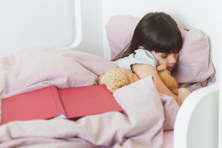 toddler girl read and looked at a book and fell asleep in her bed, childhood conceptの写真素材