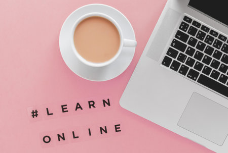 laptop, coffee cup and hashtag description learn online on pink background, e education conceptの写真素材