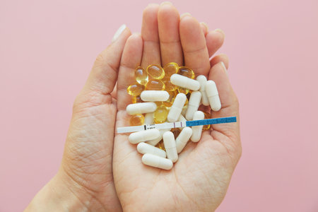 female palms on pink background with positive pregnancy test and different pills and vitamins, female health and pregnancy concept.の写真素材