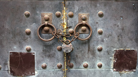 A close-up of an old metal door secured with rusty chains and a vintage padlock, featuring heavy...