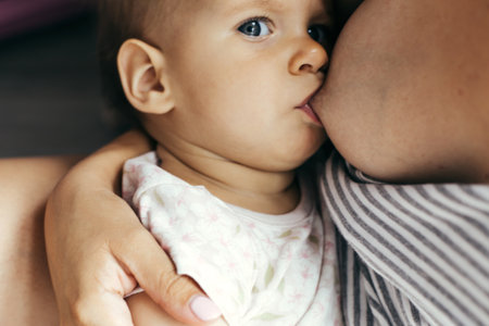 Baby breastfeeding in mother's arms close-up indoors, concept of motherhood, theme of care, bonding, nutrition, family life.の写真素材
