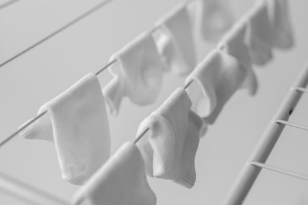 Close-up of white baby socks hanging on a drying rack indoors, monochrome image with soft light and shallow depth of field, concept of childhood and domestic careの写真素材