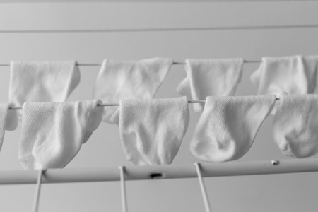 White baby socks neatly hanging on a drying rack indoors, arranged in rows, black and white...