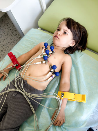 Young child undergoing ECG examination lying on medical bed with electrodes attached to chest and...