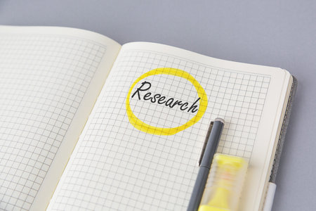 Open squared notebook with handwritten word research circled in yellow marker, pen, highlighter and coffee cup on gray background concept education and scientific workの写真素材