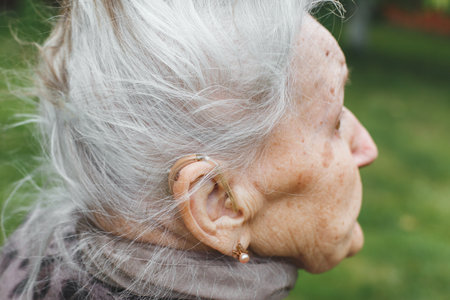 Elderly woman 80-90 years with hearing aid device in her ear, close-up of gray-haired senior person outdoors, concept of aging and healthcareの写真素材