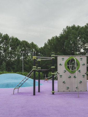 Colorful modern playground with climbing walls and structures on purple rubber surface and blue hill, surrounded by trees, concept of childhood activity and safe outdoor playの写真素材