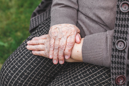 Close-up of elderly woman s wrinkled hands resting on lap in peaceful pose, wearing warm clothing, concept of aging and life experienceの写真素材
