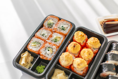 Assorted sushi set in plastic containers: salmon and avocado rolls, baked rolls with cheese topping....