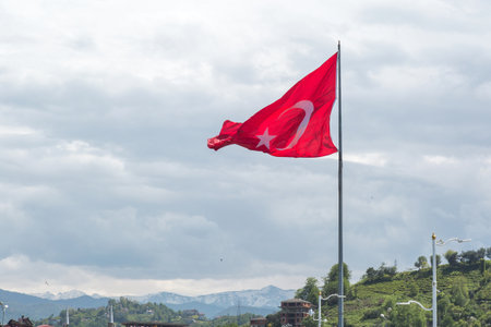 Turkish national flag waving on a pole against mountain and cloudy sky, concept of patriotism and national identity.の写真素材