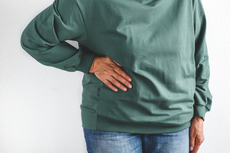 Close up of senior woman in green hoodie and jeans holding her side suffering from flank or...