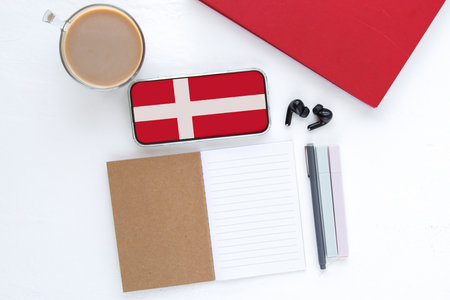 Smartphone with Denmark flag on screen, open notebook, coffee cup and stationery on white table, concept of online language learning, education and studying Danish cultureの写真素材