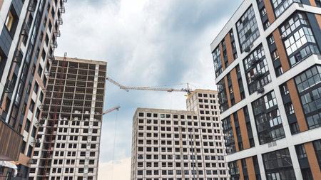 Modern urban residential buildings under construction with cranes between high-rise structures, cloudy sky background, symbolizing city development, architecture, and real estate growthの写真素材