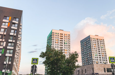 Modern residential buildings with colorful window accents under pastel evening sky, urban street with pedestrian crossings and trees, representing city architecture and comfortable living environmentの写真素材
