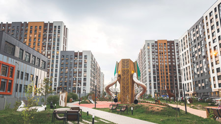Modern courtyard playground with large wooden elephant-shaped slide surrounded by benches, greenery and high-rise residential buildings, representing creative urban design and family recreationの写真素材