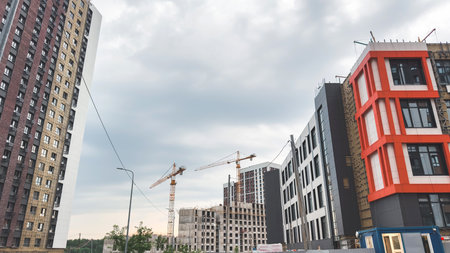 Construction site with modern residential buildings in progress, cranes working between finished and unfinished structures, cloudy sky above, symbolizing city growth, architecture urban developmentの写真素材