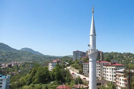 View of Rize city in Turkey with a white mosque minaret, modern residential buildings, green hills, and clear blue sky, representing culture, religion, architecture, and travel conceptsの写真素材