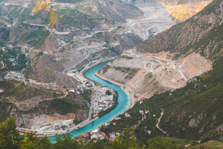 A winding turquoise river Choruq flows through the deep mountain valley near Artvin, Turkey, surrounded by rugged hills, roads, and small settlements, harmony between nature and human engineeringの写真素材