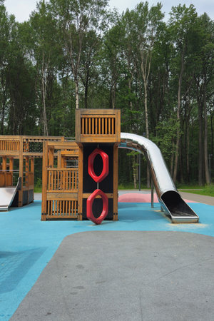 Playground with tall slide and climbing rings on colorful rubber surface in forest park, no...