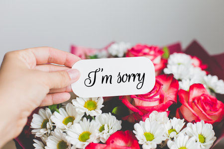 Hand holding a blank white card above a beautiful bouquet of red roses and white daisies, concept of greeting, love message, floral gift, celebration, and personalized card design. copy spaceの写真素材