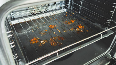 close-up view of a dirty oven interior with burnt food stains and grease on the bottom tray, showing...