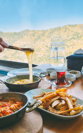 Traditional Turkish Karadeniz breakfast with muhlama, fried potatoes, tea, and local dishes served on a table with a mountain view, symbolizing culture, hospitality, and regional cuisineの写真素材