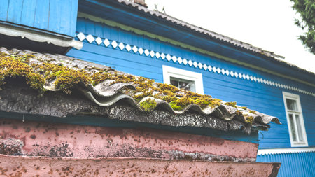 Old rural wooden house with blue walls, white window frames, and moss-covered roof, representing countryside lifestyle, rustic charm, and vintage architectural heritage conceptの写真素材