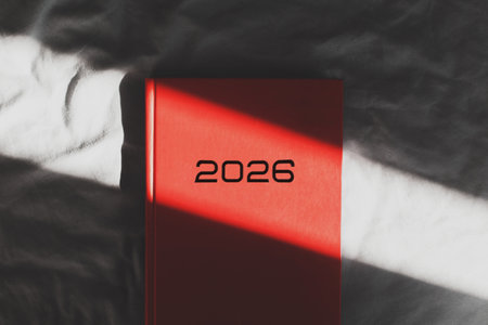Red notebook with black inscription 2026 lying on a soft surface in sunlight and shadow, concept of new year planning, goals, motivation, creativity and personal developmentの写真素材