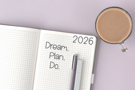 open notebook with the motivational phrase Dream. Plan. Do. year 2026 written on a grid page, next to cup of coffee and two pens on pastel lavender background, symbolizing productivity goal settingの写真素材