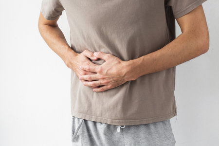 Man holding his side with both hands, feeling pain and discomfort, wearing casual clothes against a light background. Concept of side pain, internal organ issues, health problems, physical discomfortの写真素材