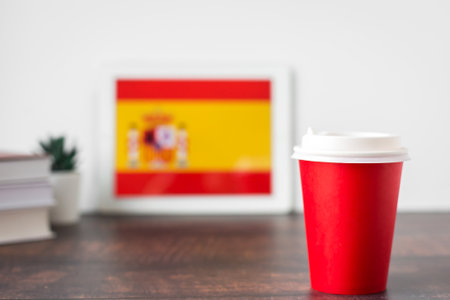 blurred background of Spain flag on tablet, textbooks, paper glass with hot drink, space for text, concept of learning Spanish language and Spanish culture.の写真素材
