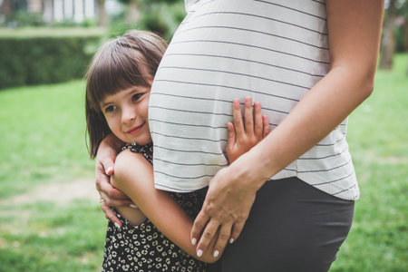 child girl 5 years old hugs mother's pregnant belly in the park in nature in summerの写真素材