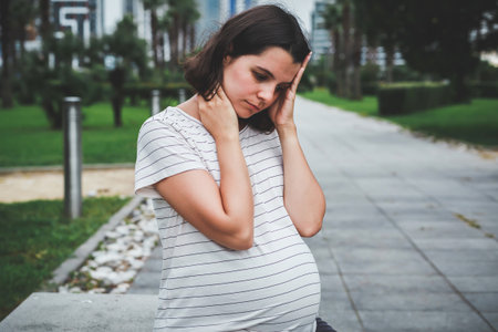 a sad pregnant woman sits alone on a bench in the park in summerの写真素材