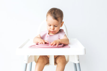 baby sits in a high chair eats complementary foods on a white background, space for text.の写真素材