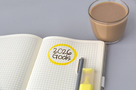 Open notebook with grid pages showing handwritten words 2026 Goals circled in yellow, next to pen, highlighter, and cup of coffee gray surface, symbolizing planning, focus, and future success conceptの写真素材